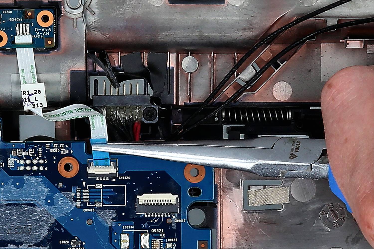 'Close-up of a motherboard: A hand uses pliers to connect a ribbon cable to a circuit board.'