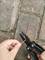 A person is holding a black multi-tool to cut a red cable on a paved surface.