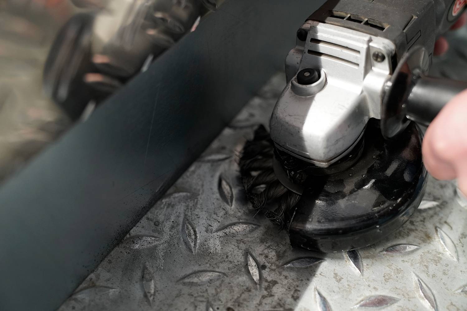 A person is grinding a metal surface with an angle grinder. The diamond-shaped pattern on the metal is clearly visible.