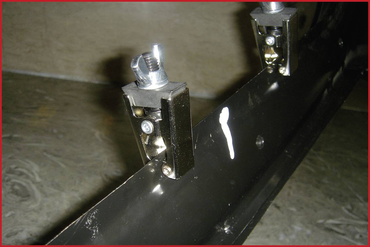 Two metal fixings on a dark, long, curved metal piece, marked with a white spot. Rustic setting.