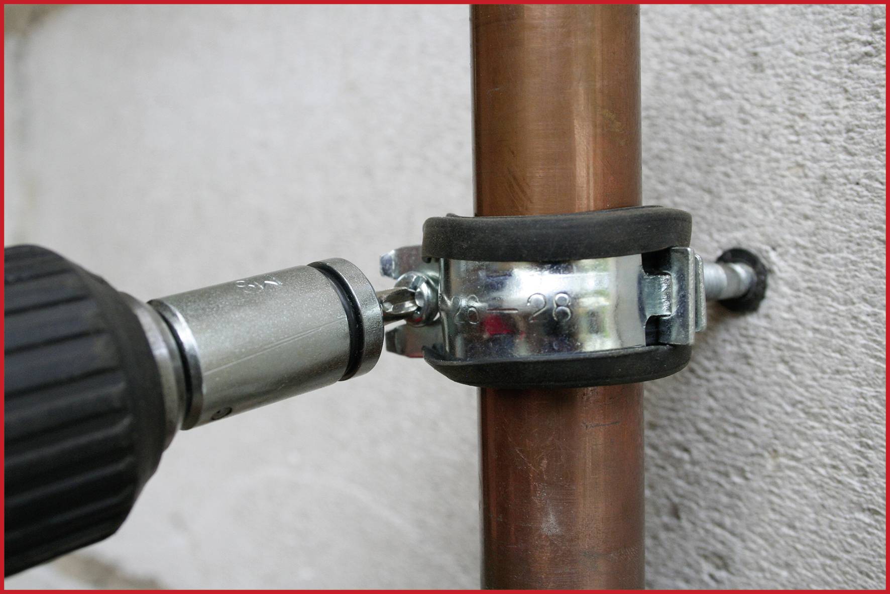 A drill pulls a screw that secures a clamp to a copper pipe.