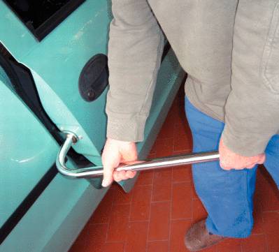 A man is using a crowbar to force open the door of a car. The car is green in colour.