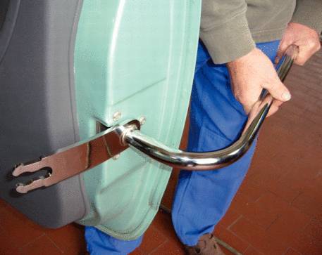 A person is fitting a metal handle to a green device, demonstrating workshop work.