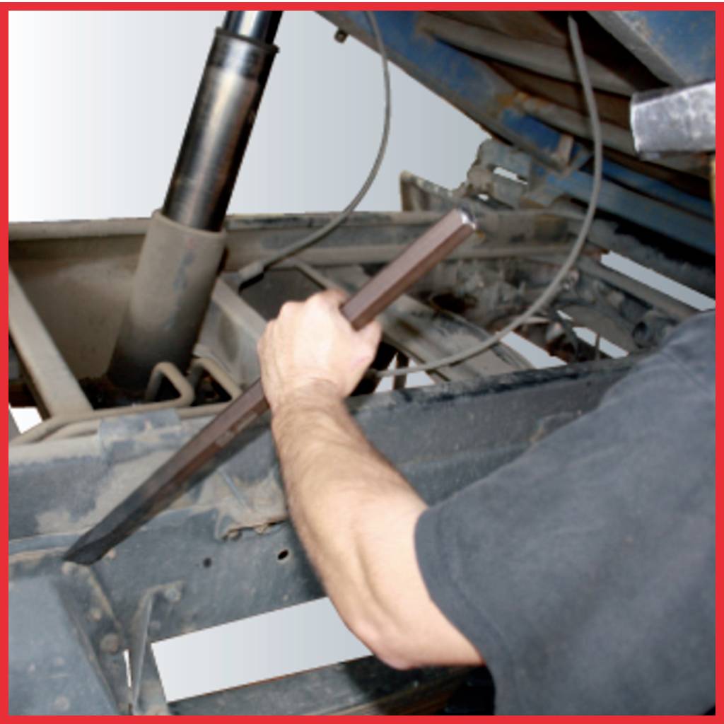 A person is operating a lifting mechanism with a metal rod on a technical device. Machine components can be seen in the background.