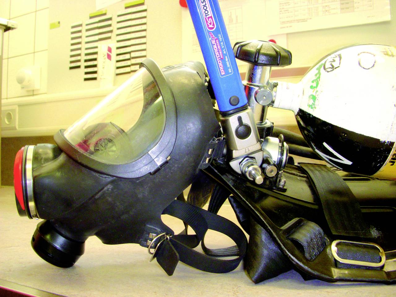 Breathing mask and oxygen tank are lying on a table in a laboratory or technical environment, signalling readiness for use.