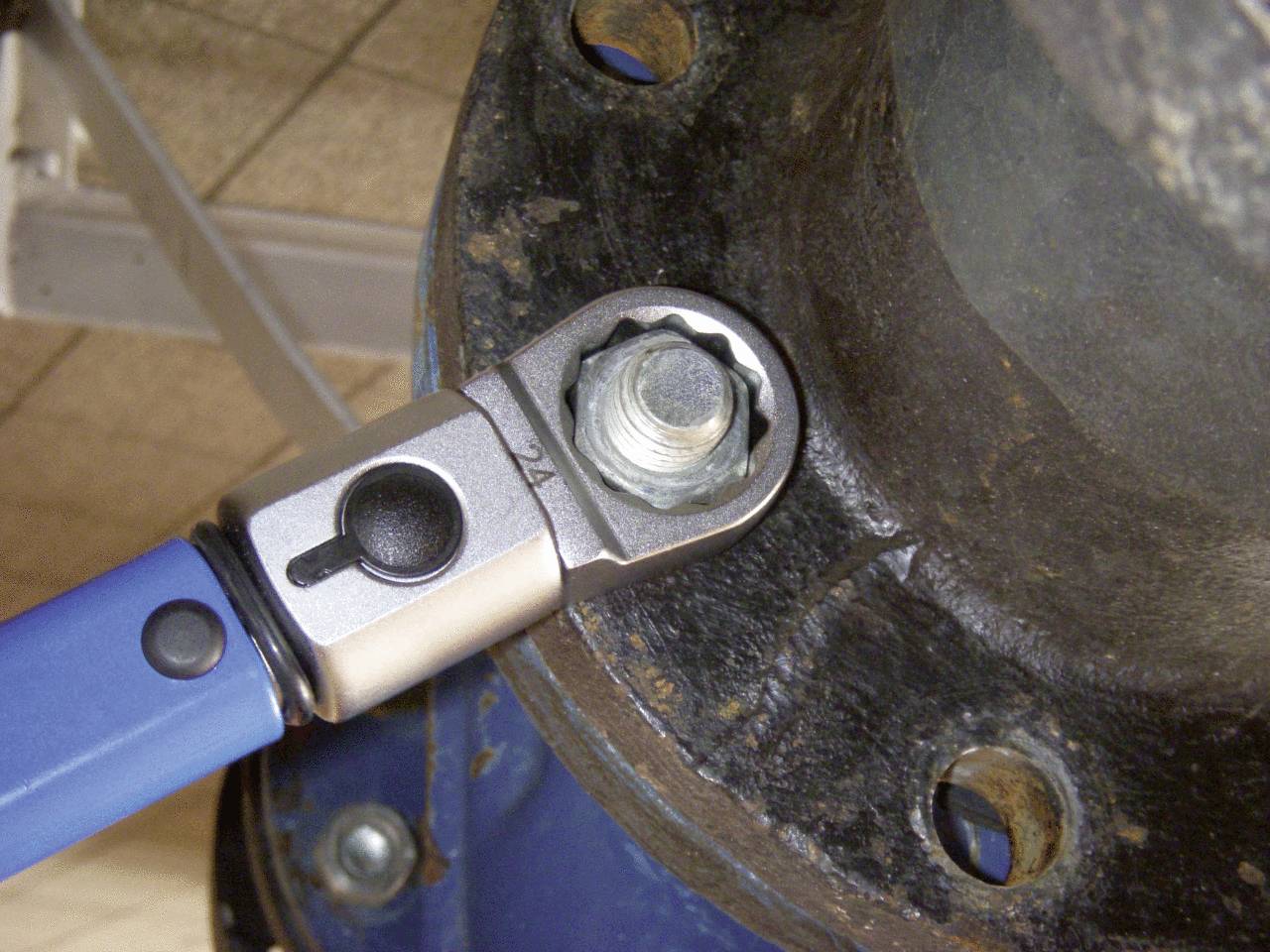 A torque wrench is tightening a screw on a metallic flange connection.