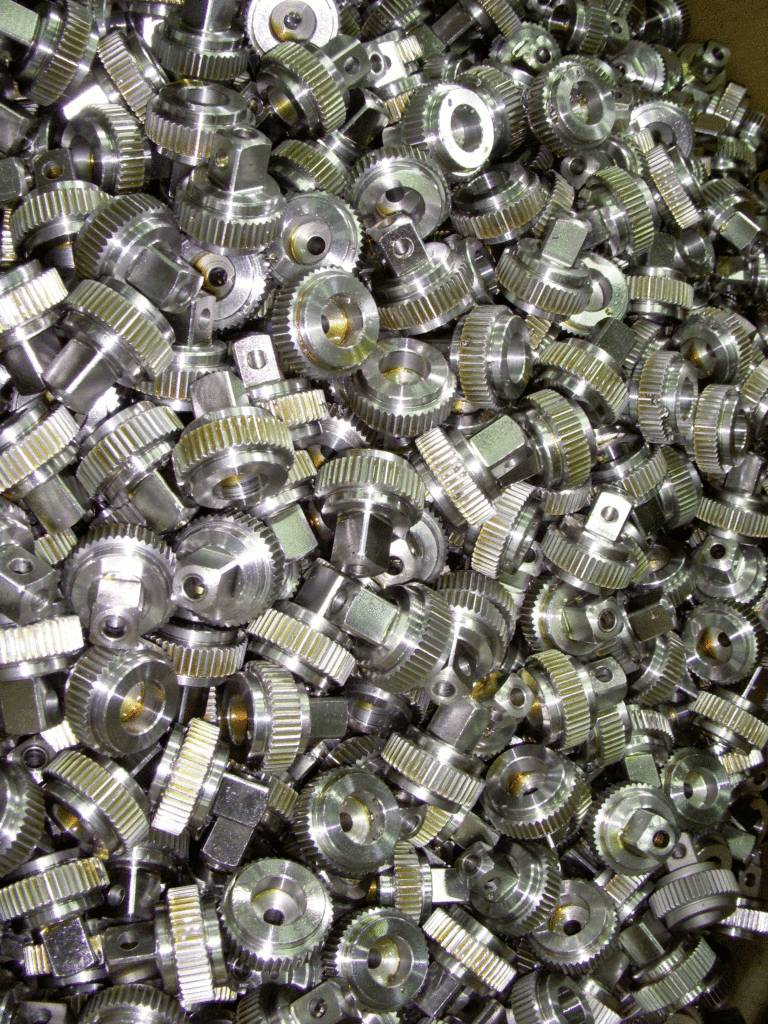 Many small metal gears in a box, tightly stacked next to each other. They display different shapes and highlights.