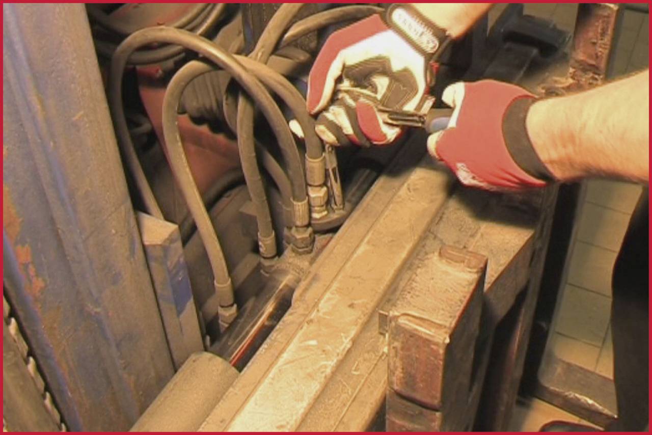 A person wearing gloves is repairing or maintaining hydraulic hoses on a heavy machine, focused intently on the task.