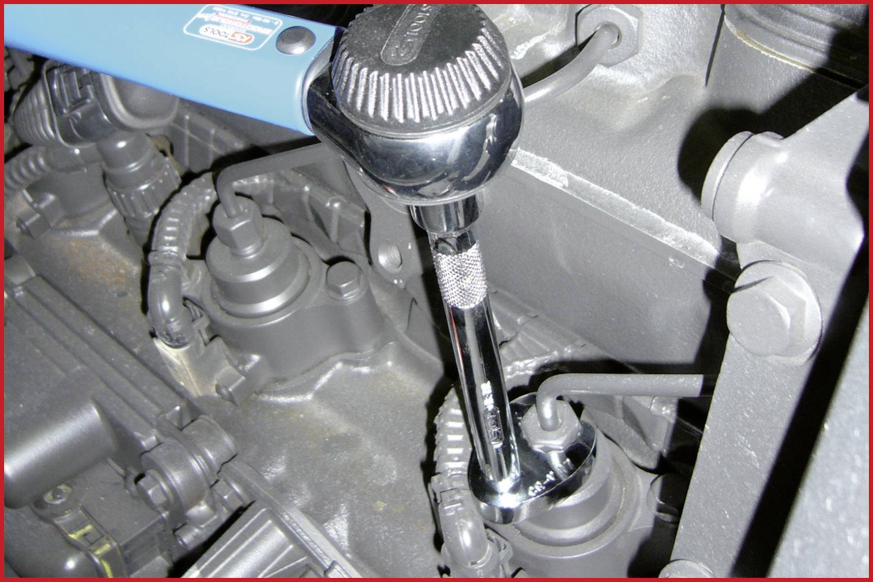 A torque wrench is used to tighten a screw on an engine block. The wrench head is positioned on a spark plug.