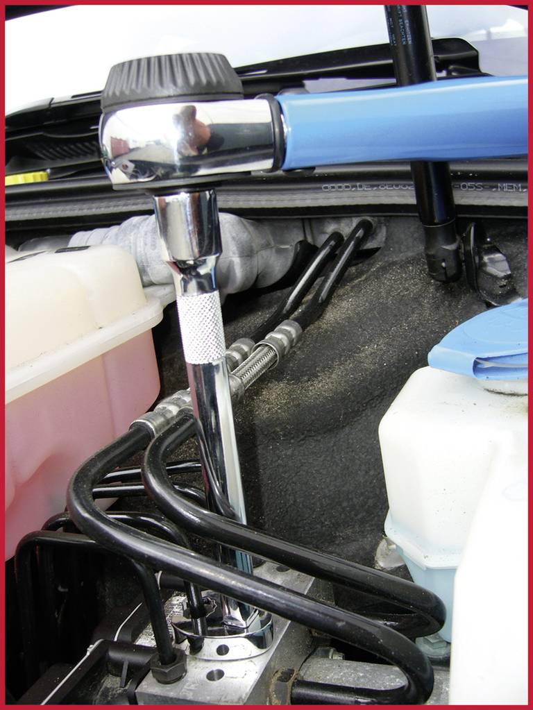 A blue torque wrench is being used under the car's bonnet to tighten a bolt. Cables and containers are visible.