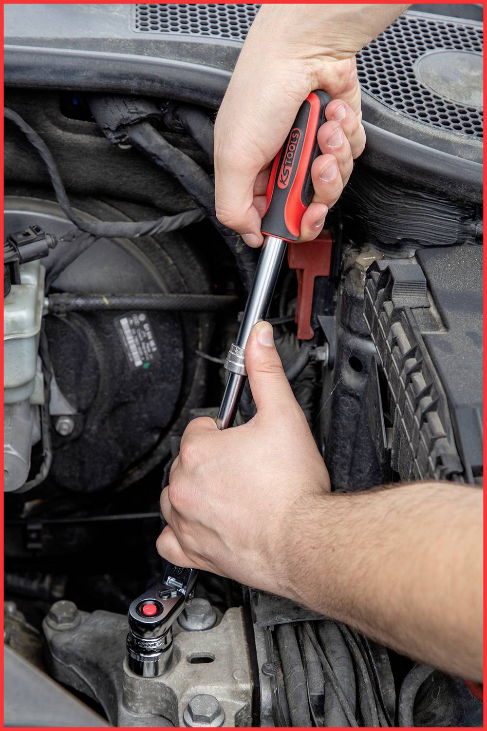 A person is tightening a screw in a car's engine bay using a spanner. Hands and tool are visible.