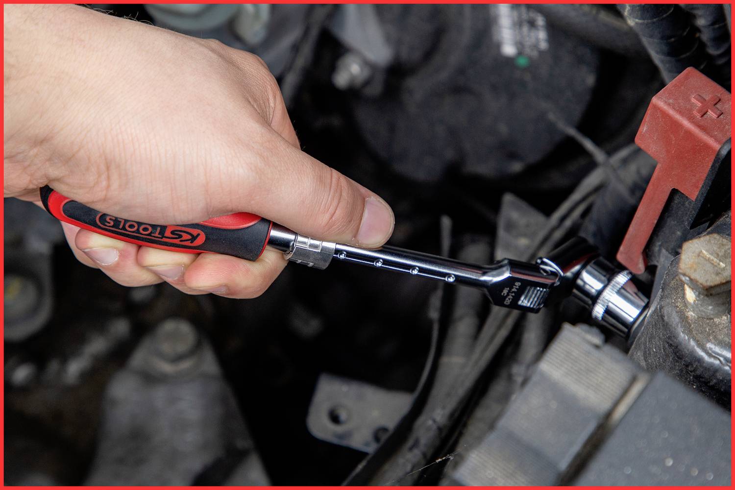 A hand is using a ratchet spanner to secure a nut in an engine compartment. The spanner bears the 'KS TOOLS' logo.