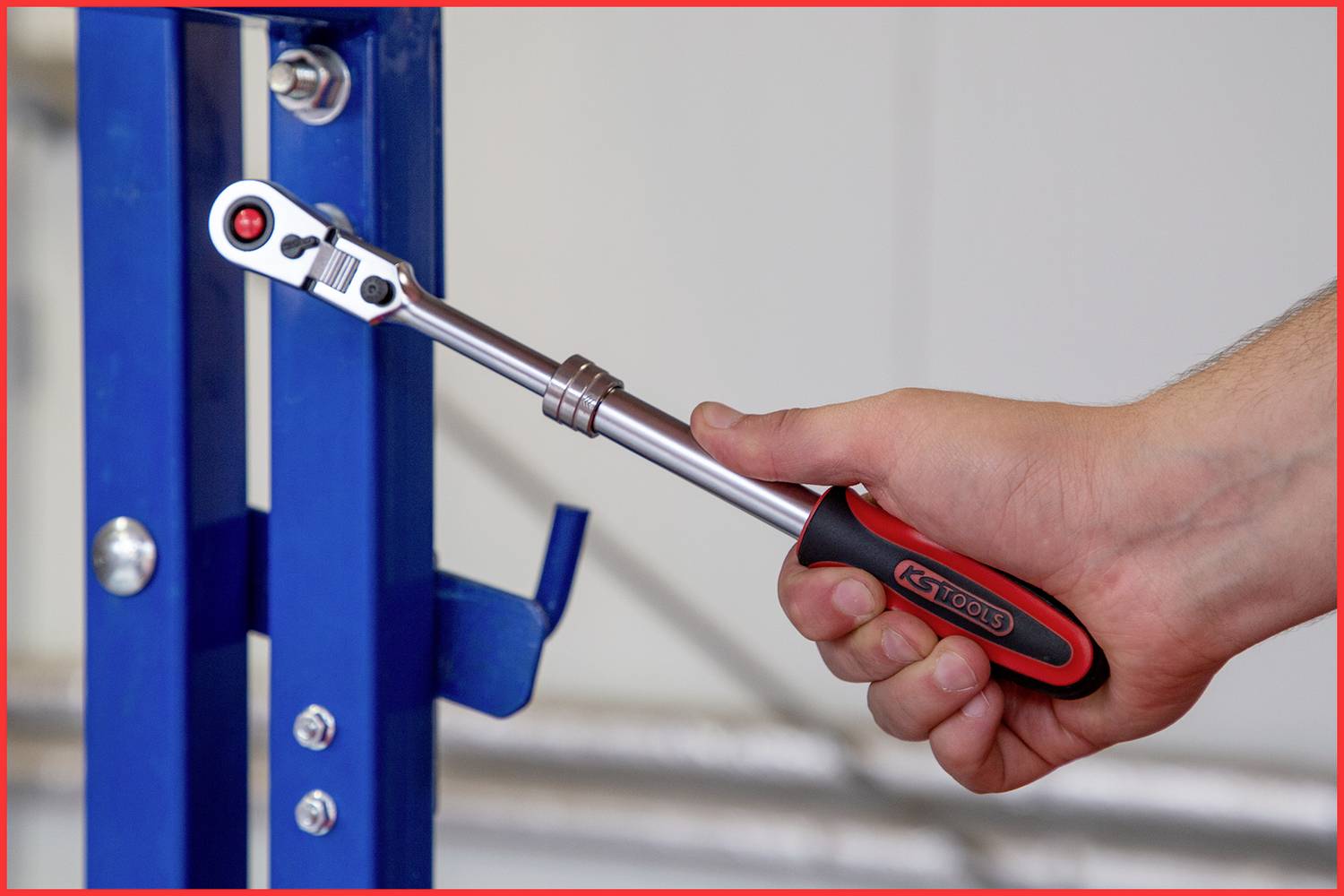 A hand holds a ratchet spanner and adjusts a screw on a blue metal structure with a precise turn.