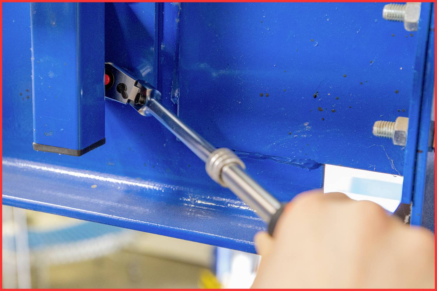 A hand is tightening a screw with a screwdriver in a blue metal construction.