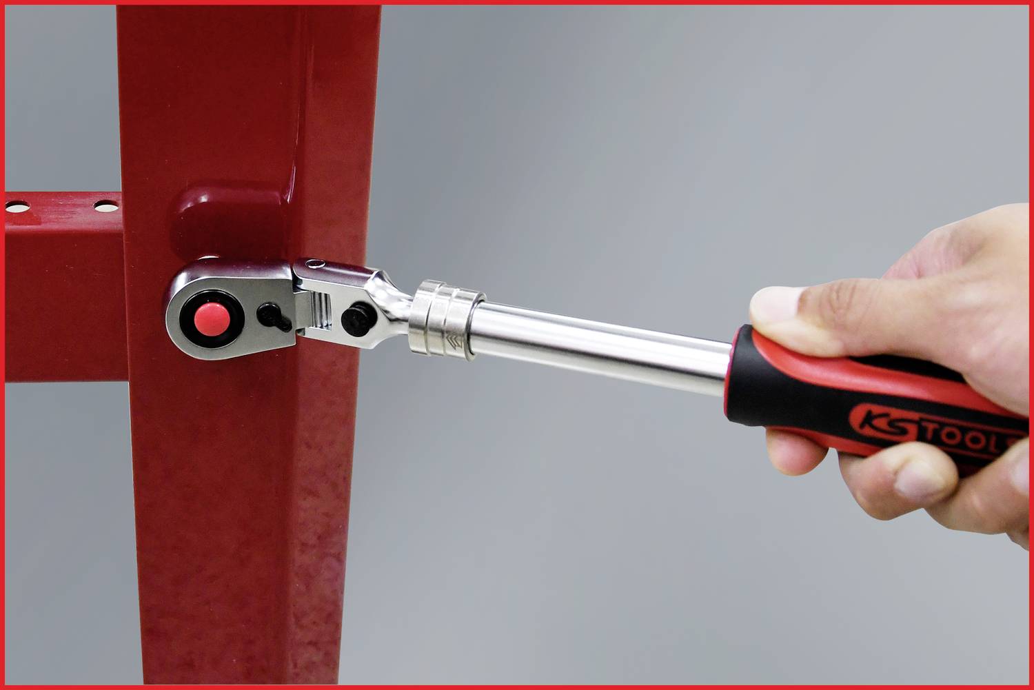A hand holds a torque wrench by KS Tools and tightens a screw on a red metal frame.