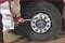 A person wearing red gloves is tightening the wheel nuts of a large lorry tyre using a spanner.