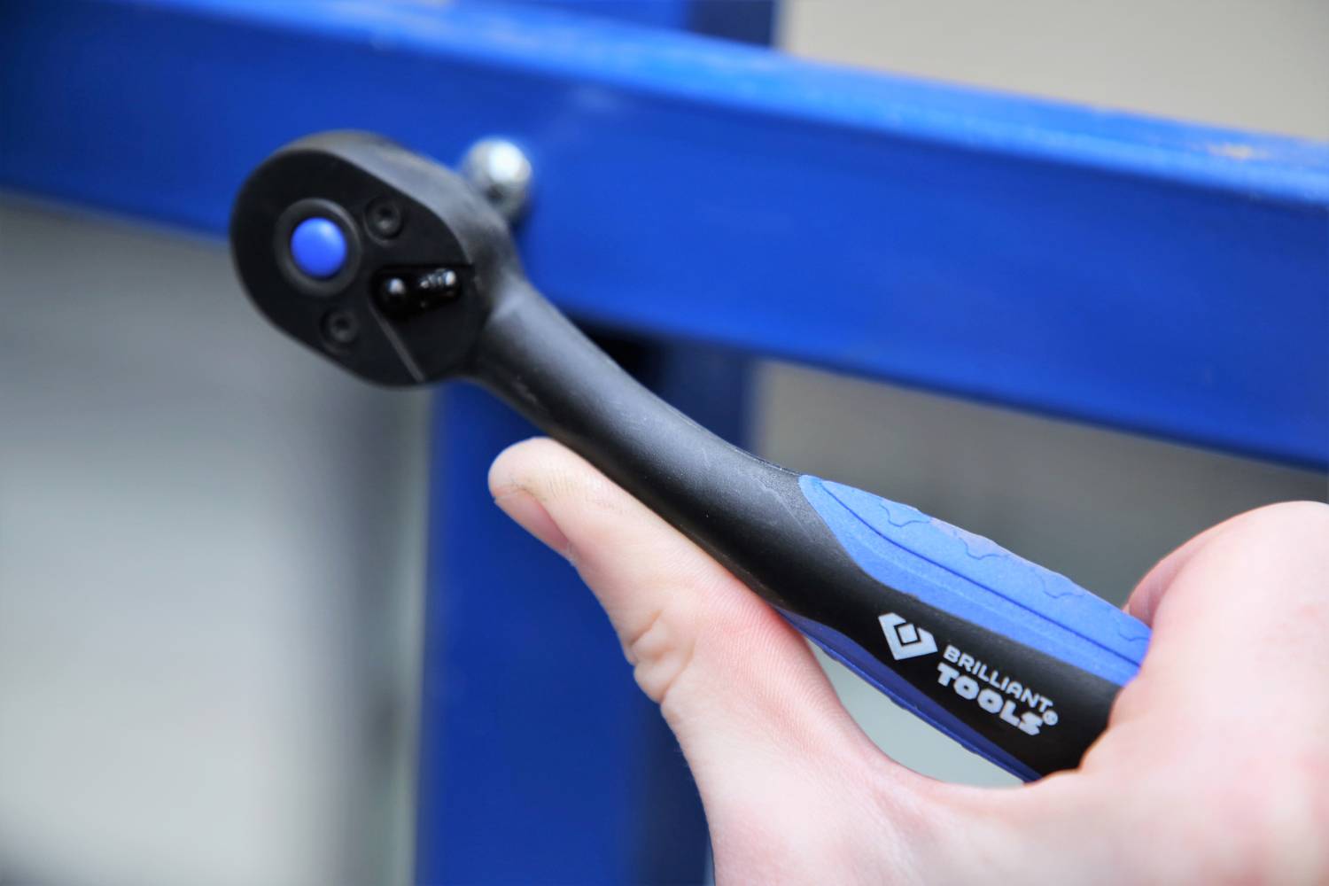 A hand is holding an adjustable wrench working on a blue metal frame. The focus is on the spannung tool.