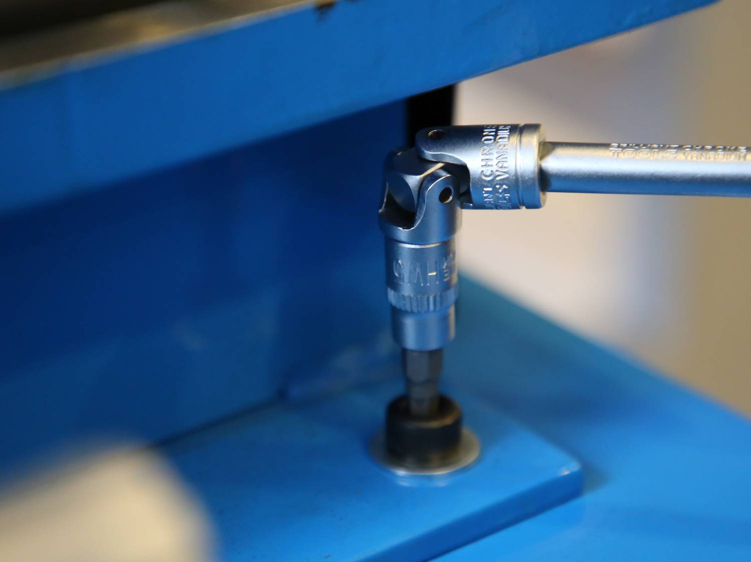 A socket spanner is placed on a screw to fasten it. The scene shows a blue background with a metal attachment.