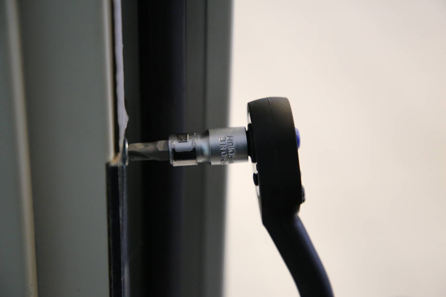 A screwdriver tightens a screw at the edge of a metal frame.