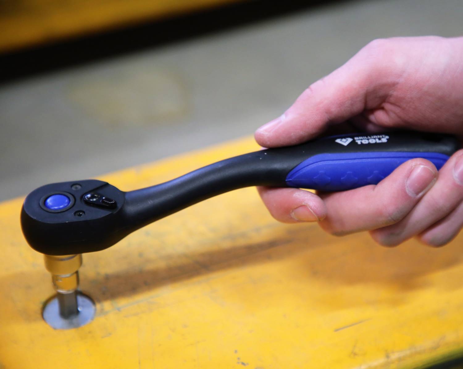A hand is using a torque wrench to tighten a screw on a yellow surface.