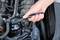 A hand uses a ratchet spanner to tighten a nut on a car part in the engine bay.