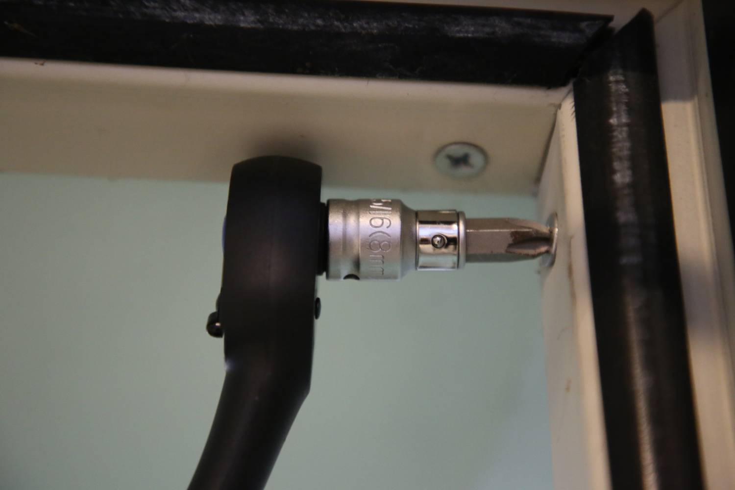 An Allen key head is attached to a screwdriver bit and is driving a screw into a door hinge.