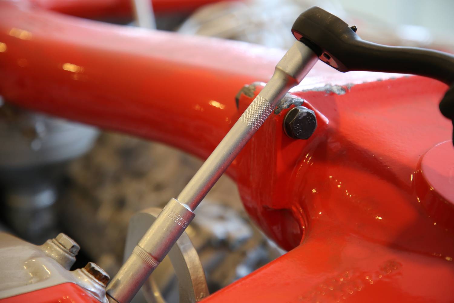 Close-up of a red vehicle with a spanner positioned against it. Focus is on the tool application.