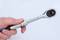 A hand holds an adjustable spanner in close-up, against a white background.