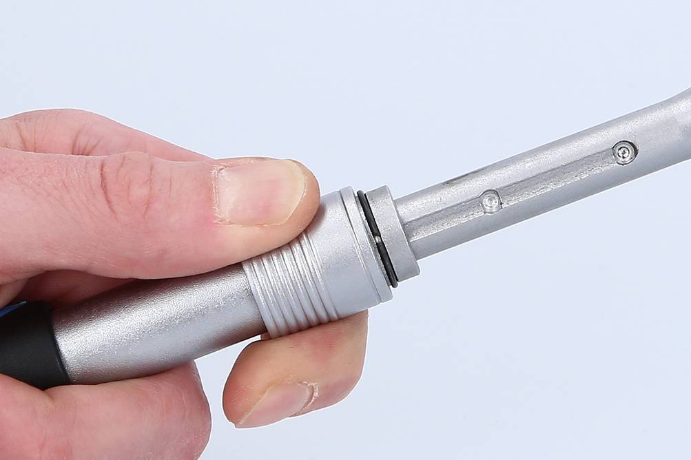 A hand is holding a silver, cylindrical metal plug against a neutral background.