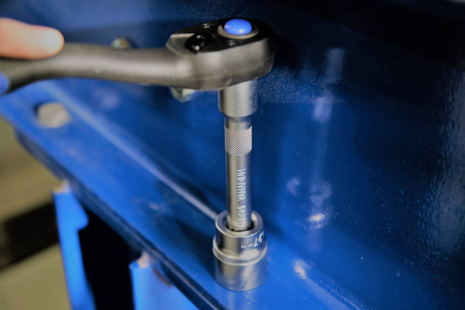 A craftsman is using a ratchet to tighten a blue metal component. The ratchet has a blue button on top.