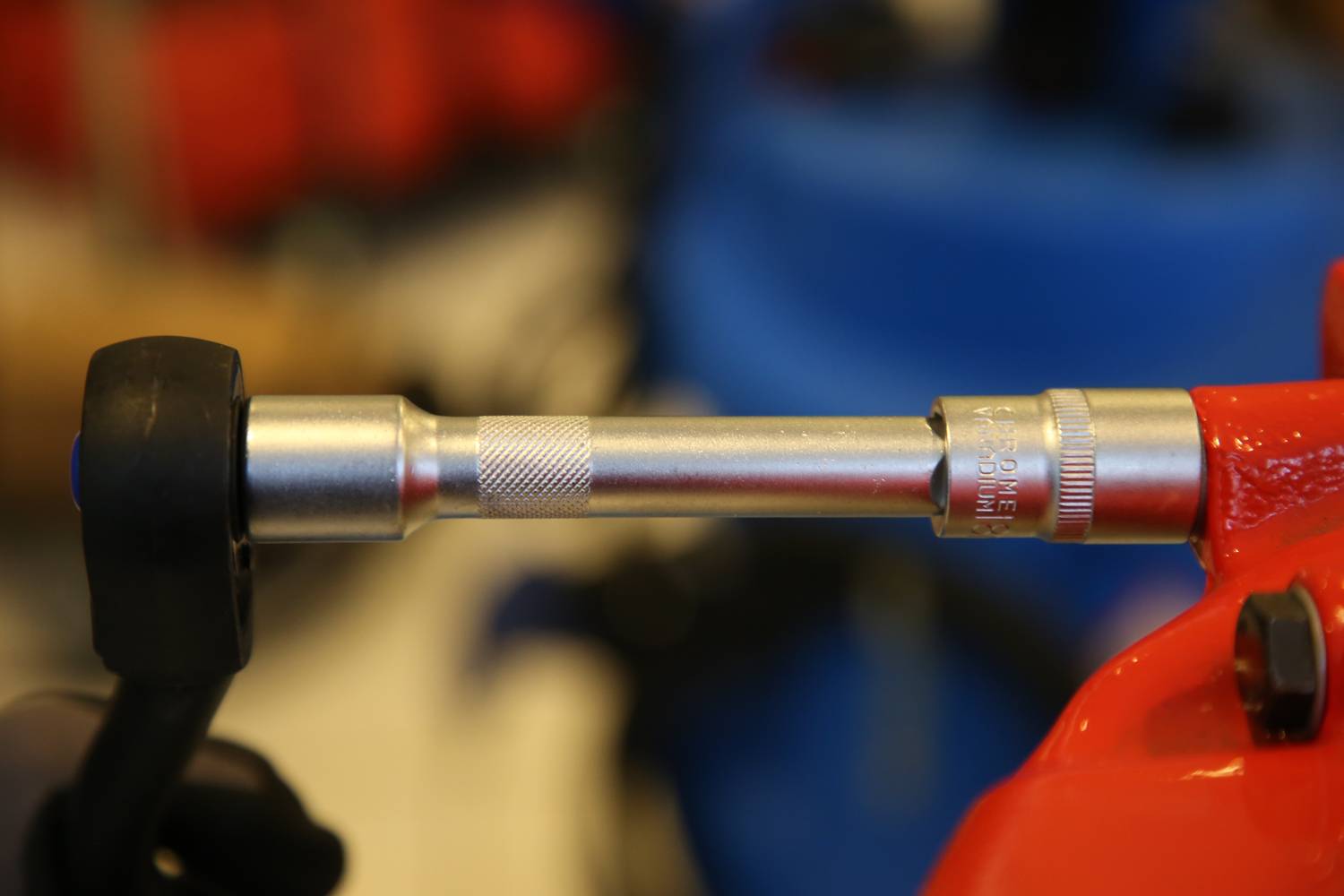 A metal rod is inserted into a ratchet-like device with red and blue elements in the background. The focus is on the tool.