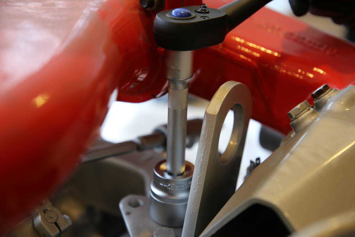 A torque wrench tightens a screw in an engine block, surrounded by red and silver metal components.