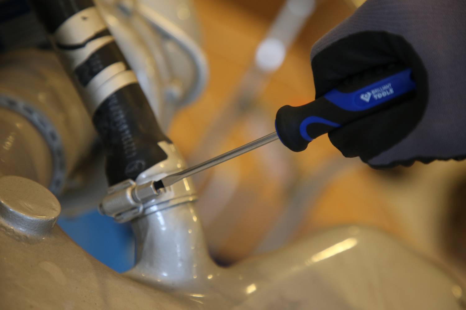 A person is tightening a hose clip with a screwdriver, presumably on a pipe.