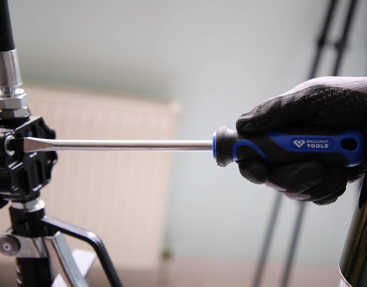 A gloved hand uses a screwdriver to turn a screw on a metallic device.