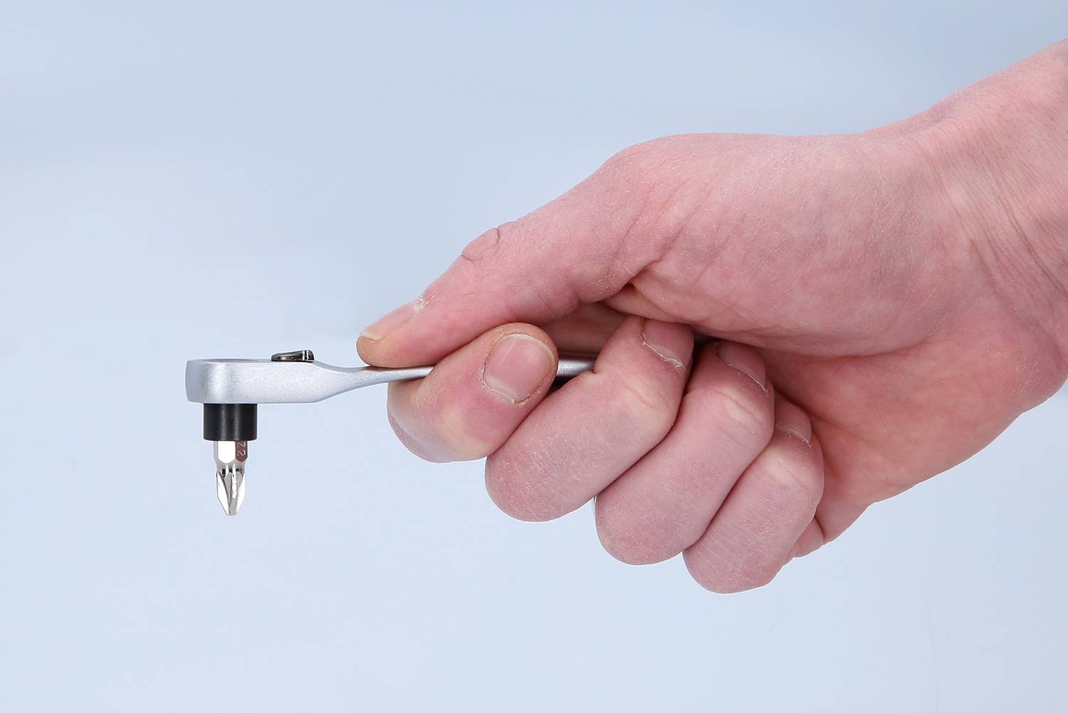 A hand is holding a small silver ratchet screwdriver, ready for use.