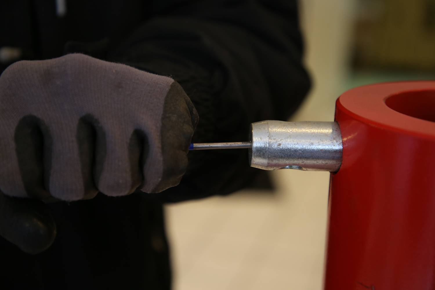 A person is holding a metal object in a red container while wearing gloves.