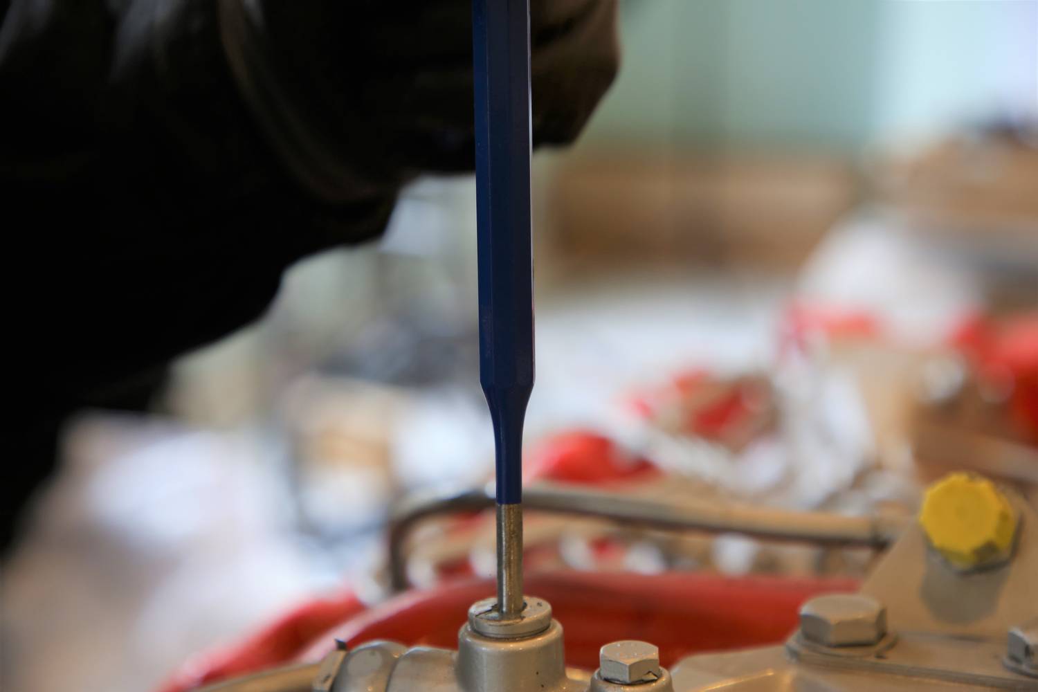 A person is repairing or assembling a mechanical component with a blue screwdriver. Workshop details are blurred in the background.