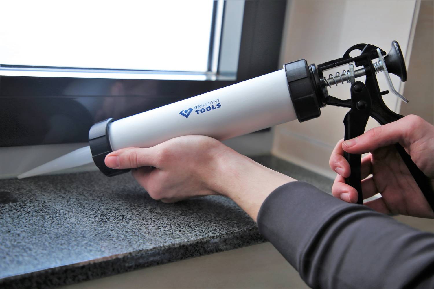 A person with a caulking gun is applying sealant to a window frame joint to ensure sealing and protection.