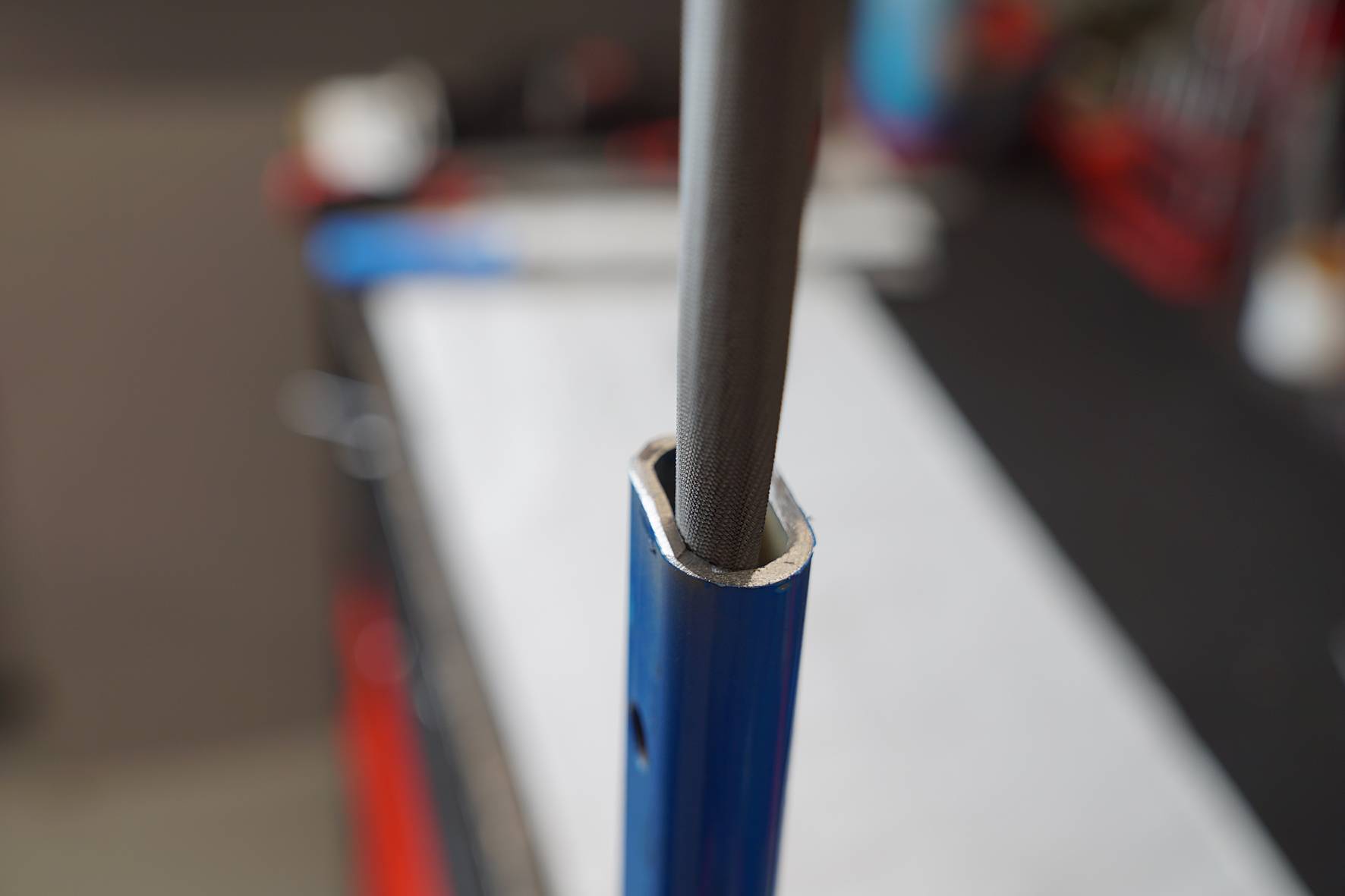 A grey cable is routed through a blue pipe. The scene is set in a workshop with blurred tools in the background.