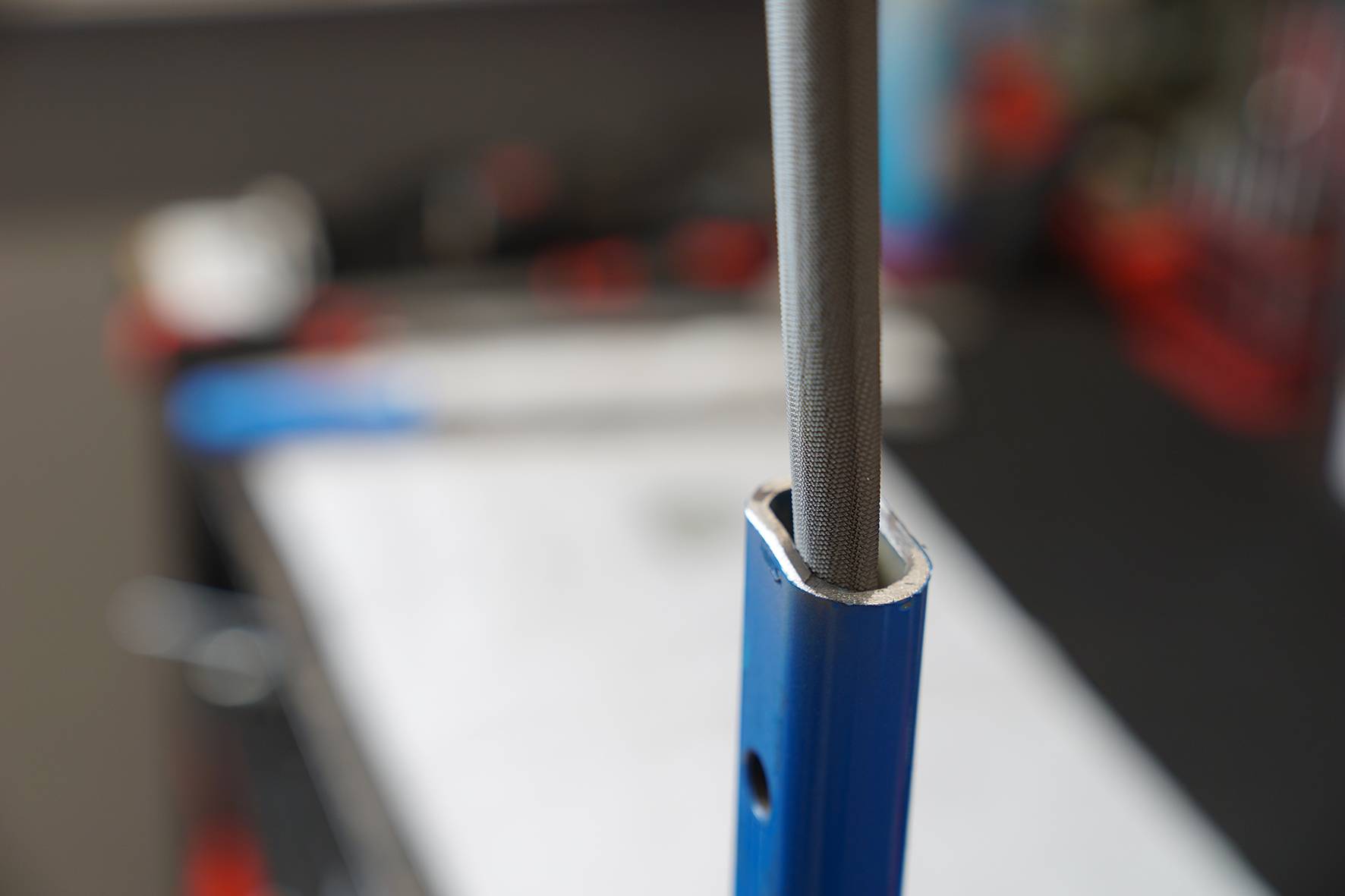 A blue pipe with a metal rod inside, against a blurry background, likely in a workshop.