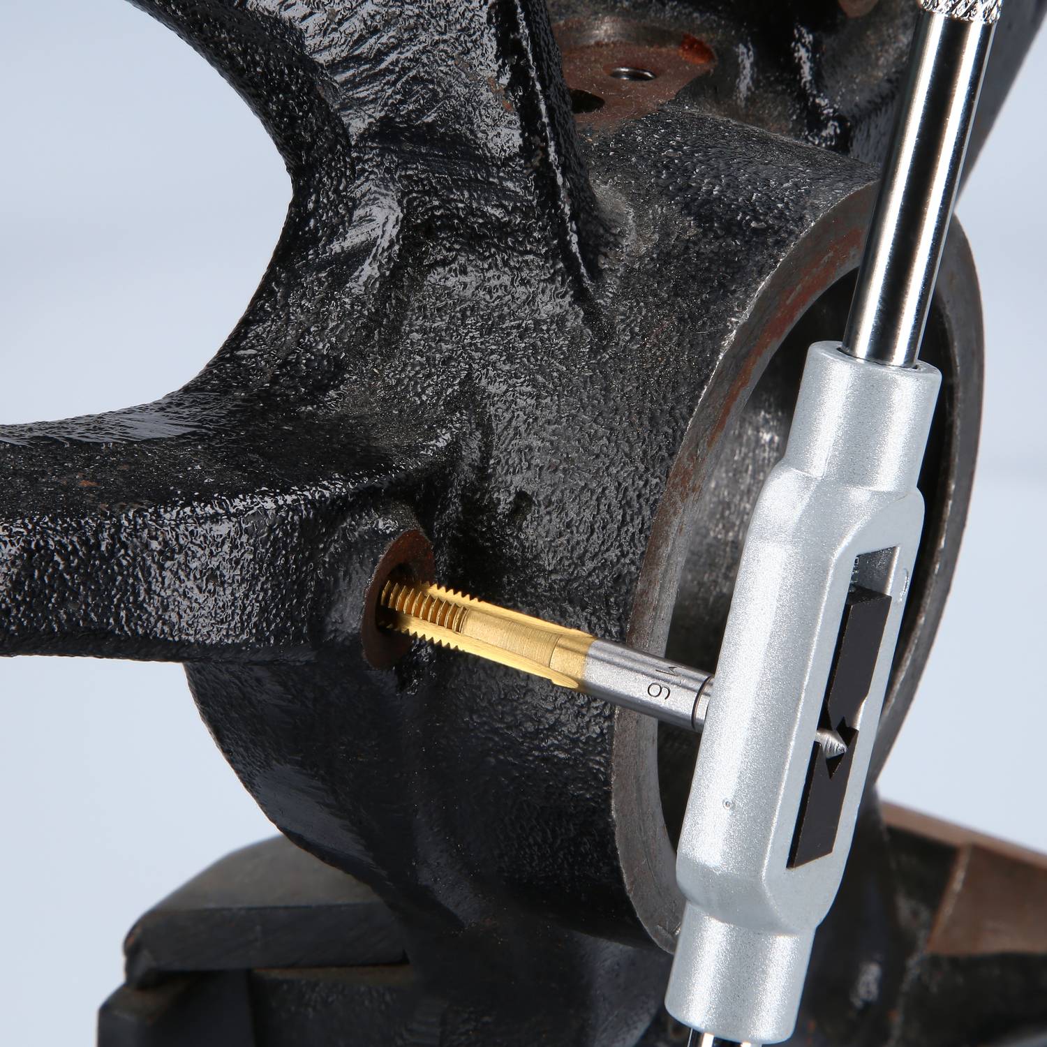 A thread cutter is cutting a new thread into a metal component that is clamped in a vice.