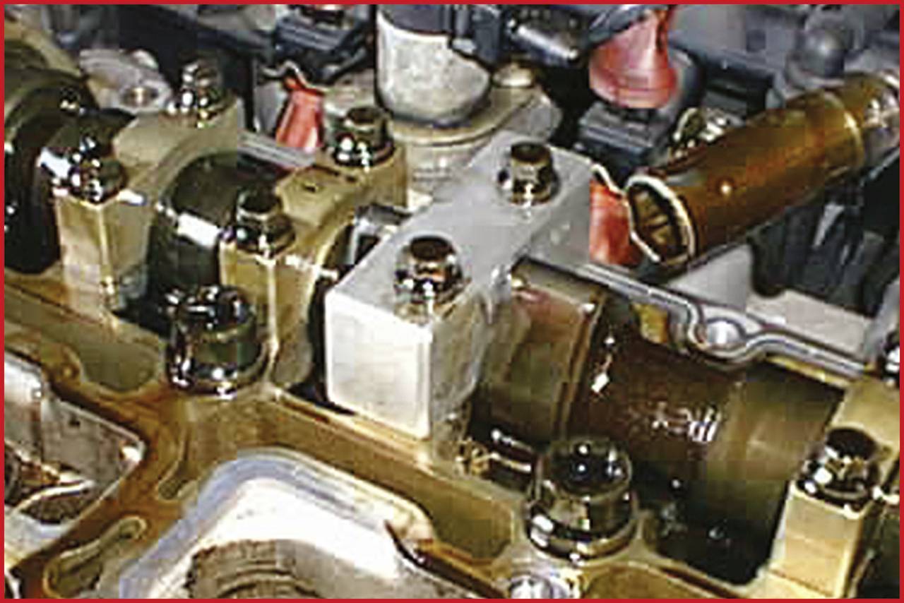 Close-up of a car part in the engine bay, focusing on a camshaft and valve control components submerged in oil.