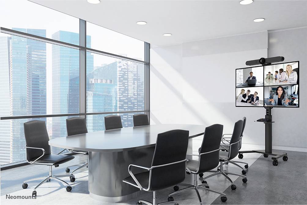 A modern conference room with an oval table, eight chairs and a large screen displaying a virtual meeting.