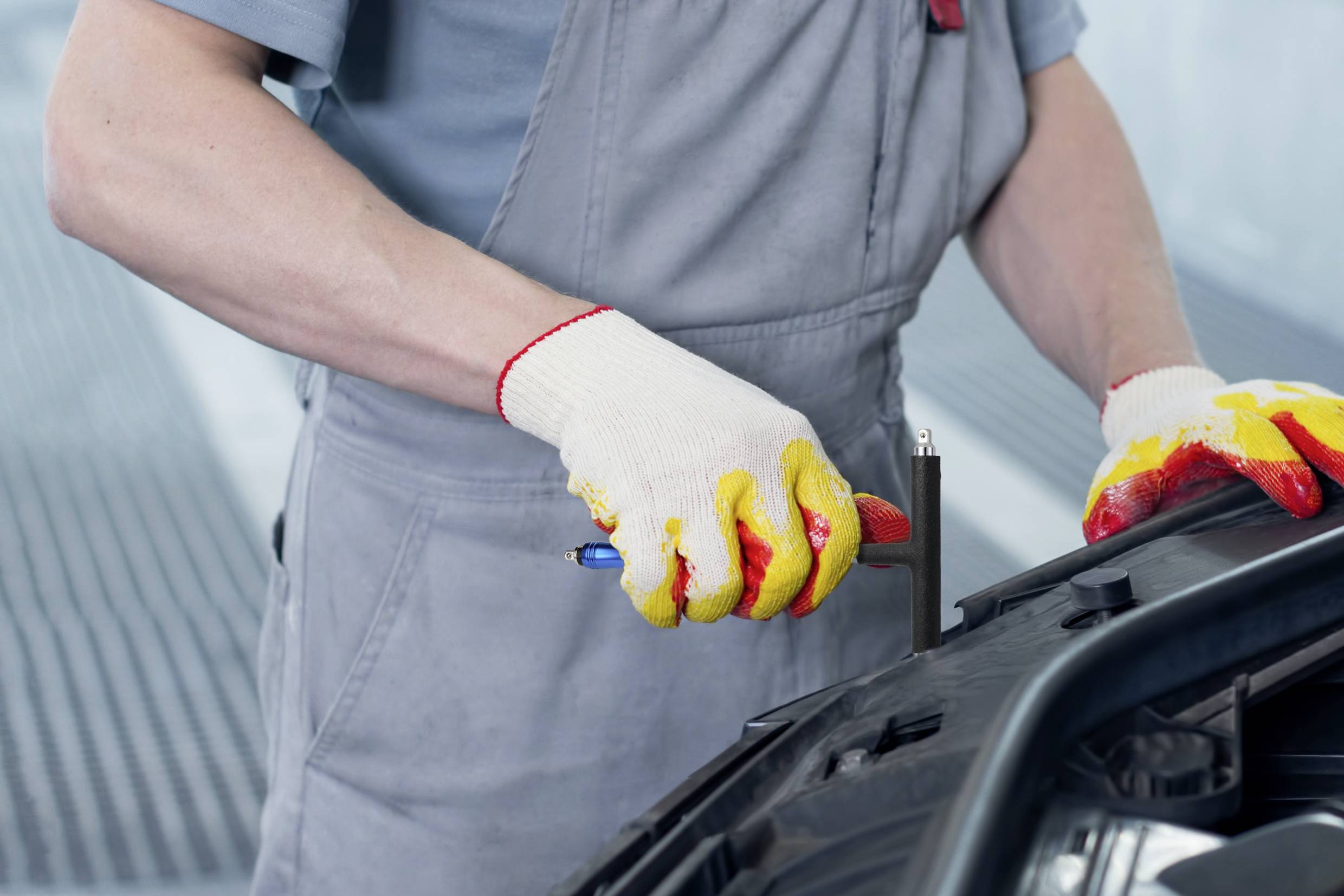 A person is repairing a car part, holding a screwdriver and wearing gloves.