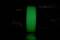 A bright green plastic filament spool in a dark environment. The spool radiates through fluorescent material under low lighting.