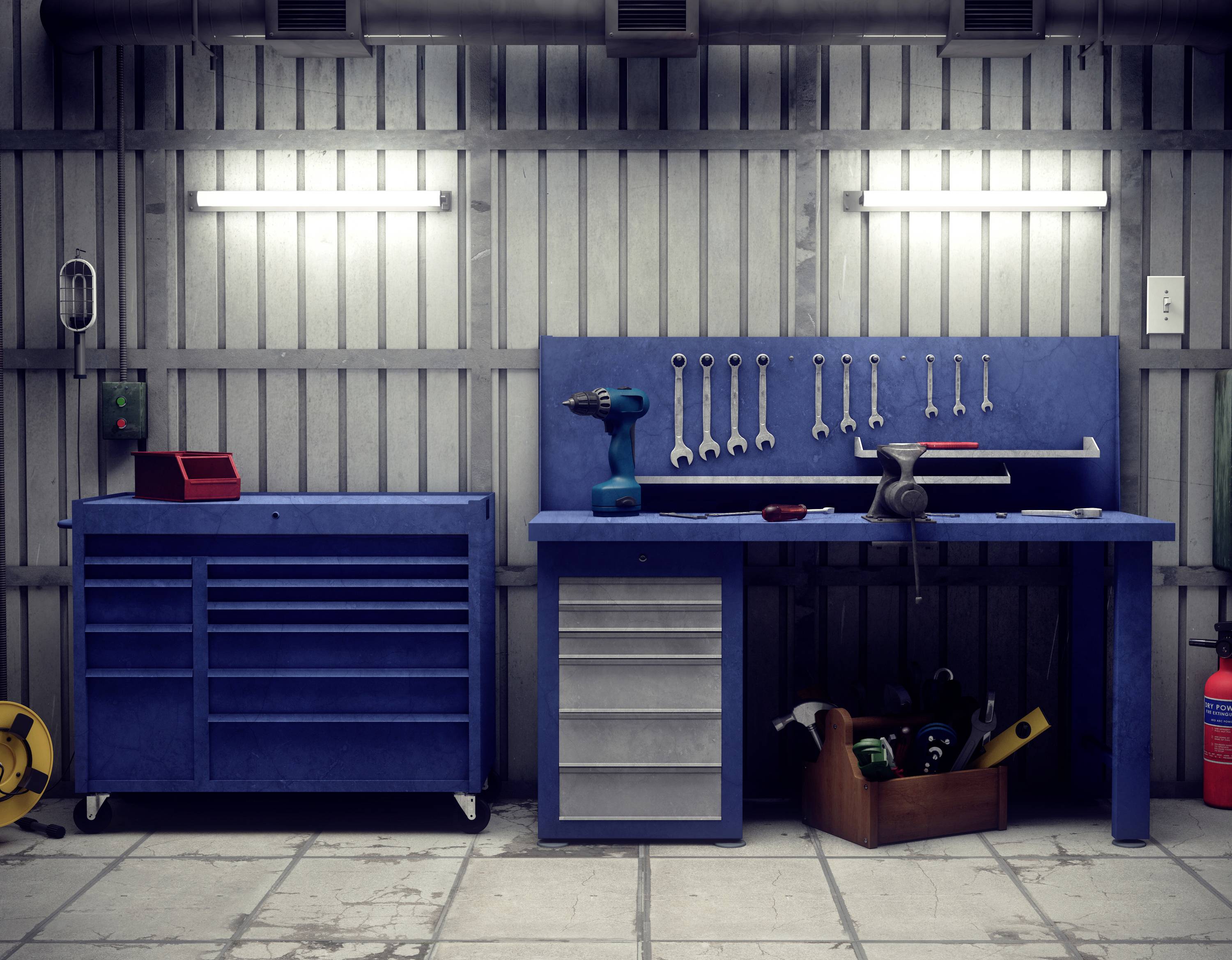 A workshop with tools on the wall, including spanners and a drill, a blue toolbox, and a workbench full of equipment.
