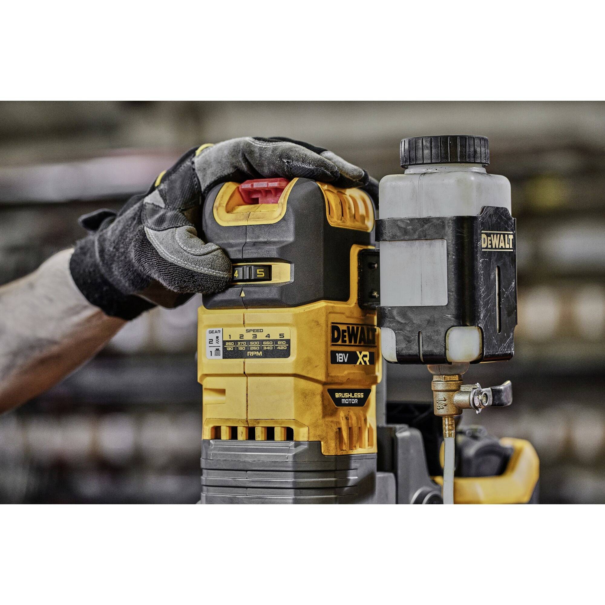 A gloved hand operates a yellow DeWalt XR power tool with an oil container. The device is being used on a workbench.