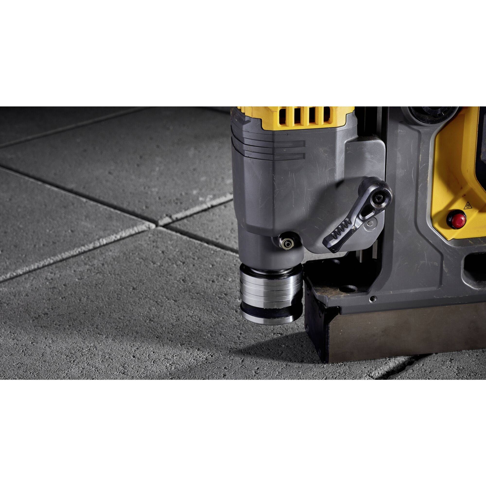 A grey drill on a concrete floor, focus on the drill head and casing. Working precisely at the edge of a concrete slab.