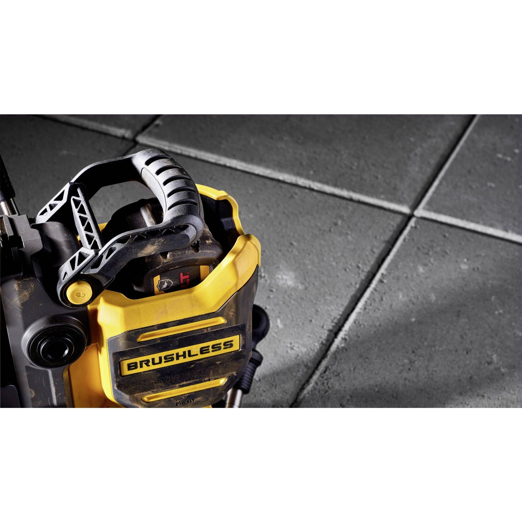A yellow, brushless drill with a black handle on grey concrete tiles. The surface of the tiles is visible in the background.