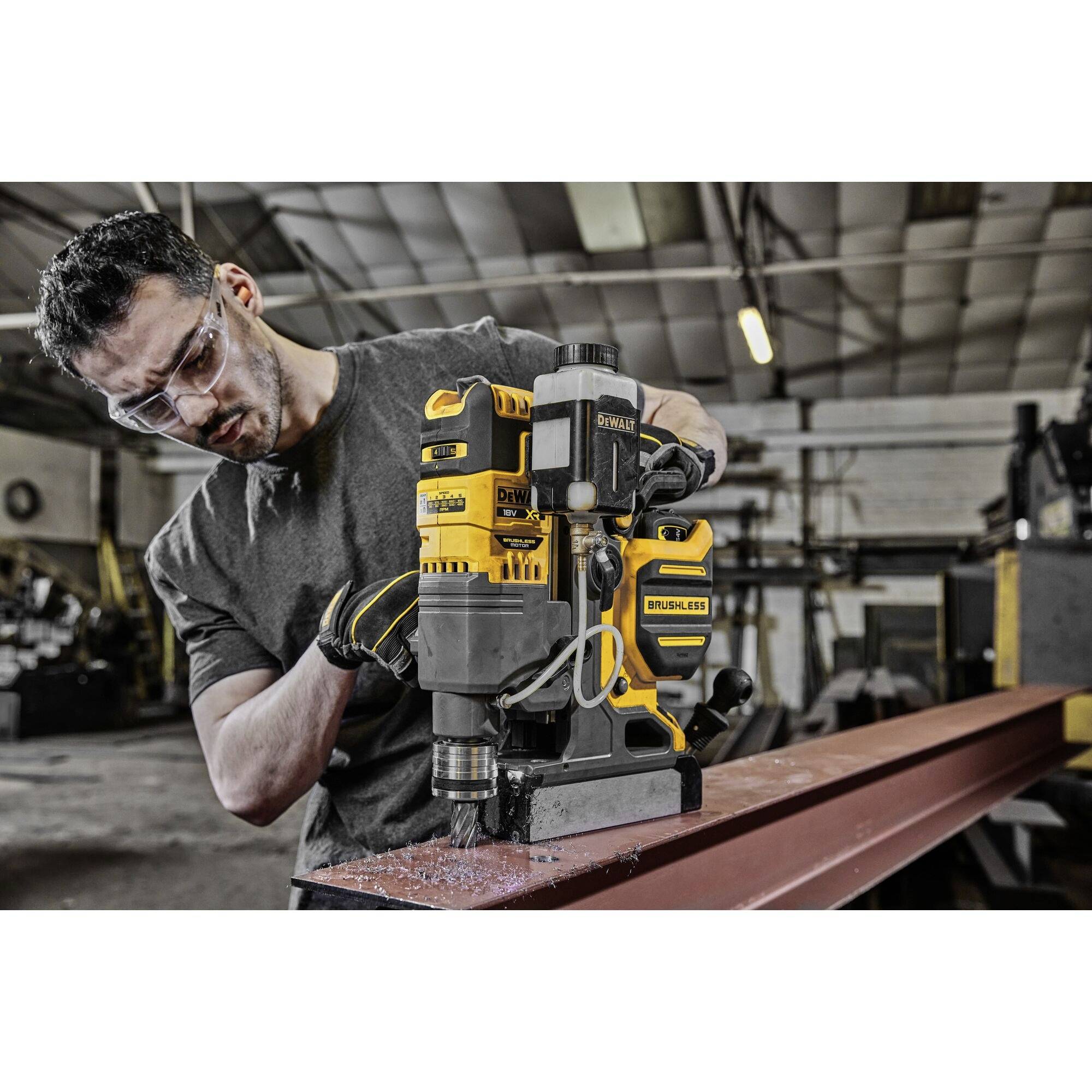 A person is drilling into a metal carrier with a yellow, brushless drill in a workshop. Safety protection is being worn.